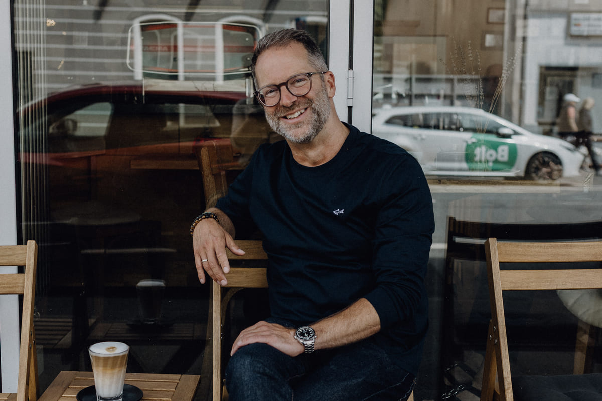 Christoph Fogel lächelt im Straßencafé – entspannt und nahbar als Coach für Klarheit und Positionierung